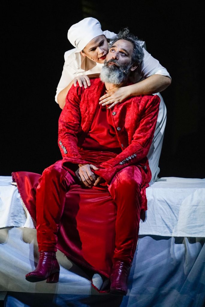 השחקנים מוריס כהן ומיה לנדסמן על הבמה במחזה "מתאבל ללא קץ". כהן לבוש אדום ולנדסמן בלבן כאחות רחמנייה