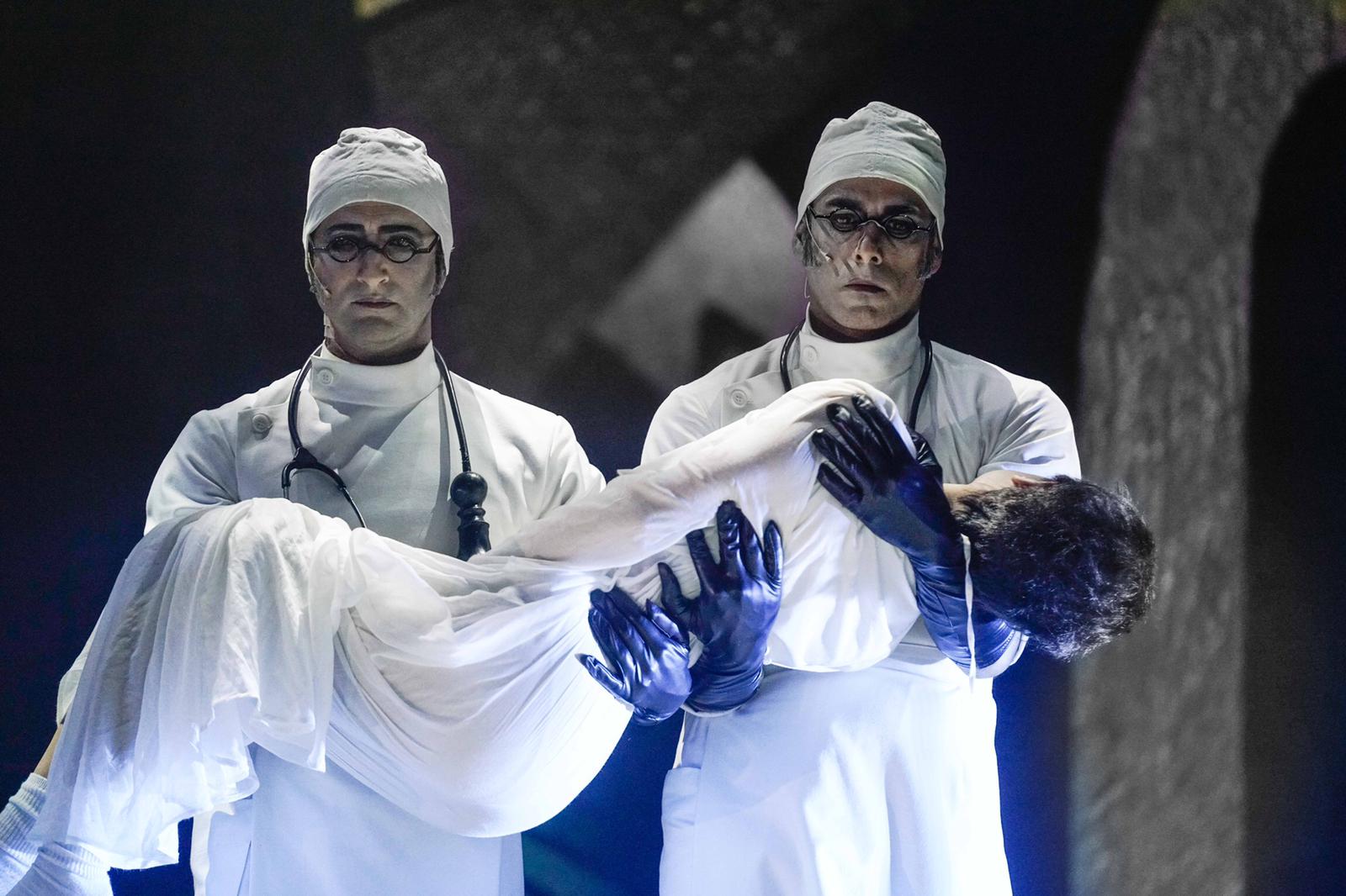 סצנה מתוך ההצגה "מתאבל ללא קץ". שני רופאים בבגדים לבנים נושאים ילד מת
