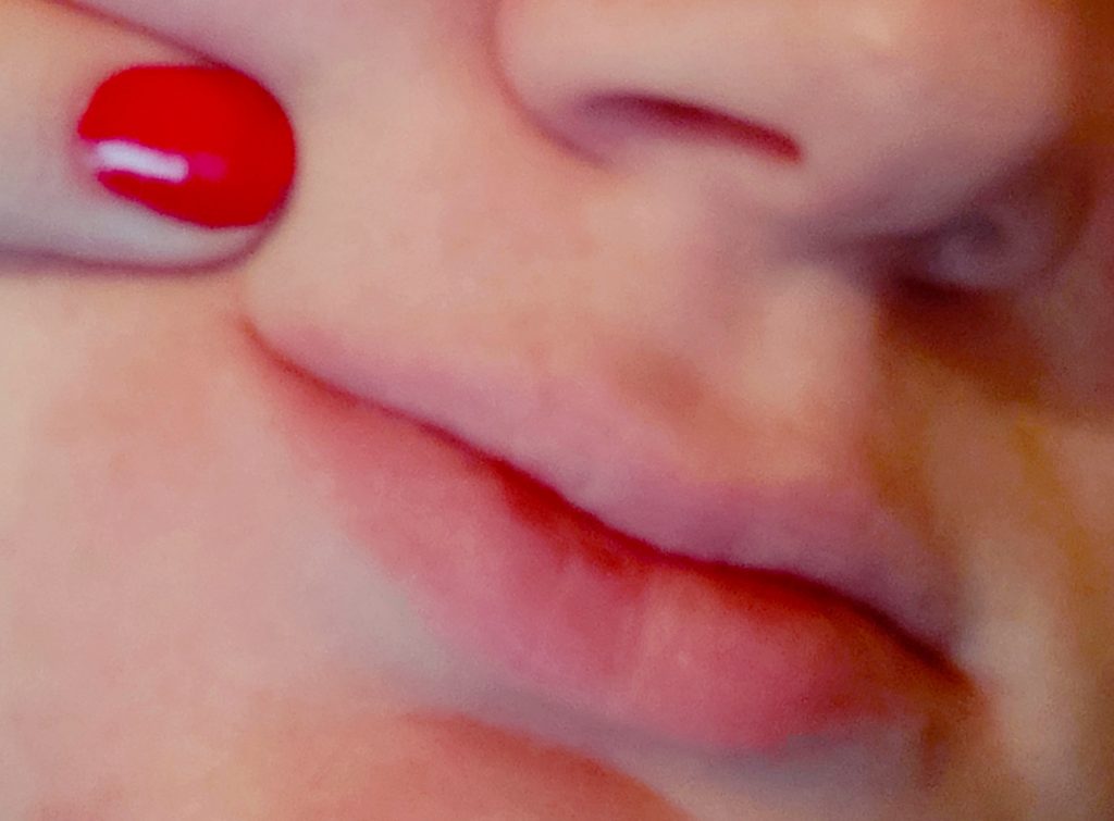 צילום תקריב של הפנים של טולי. רואים שפתיים ואף ואצבע עם לק אדום מצביעה