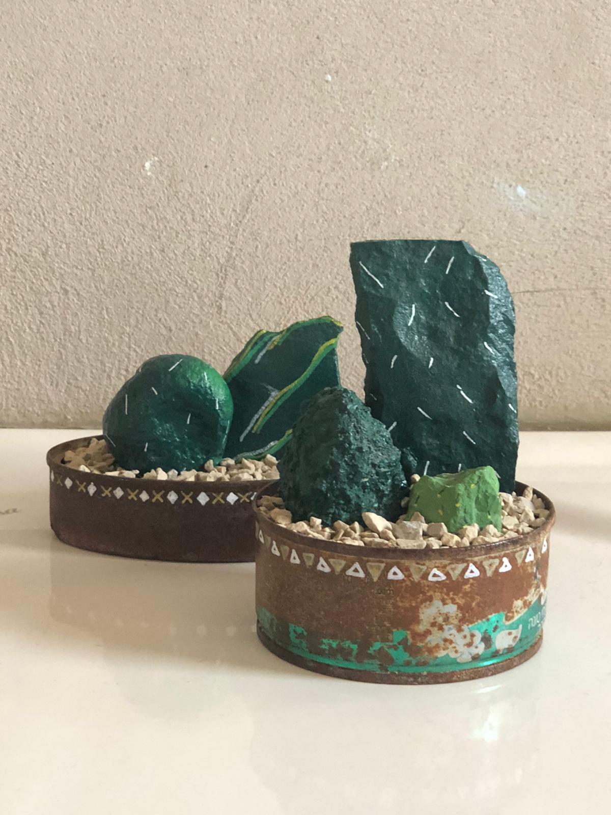 תמונה של אבנים צבועות ירוק בתוך קופסאות שימורים חלודות