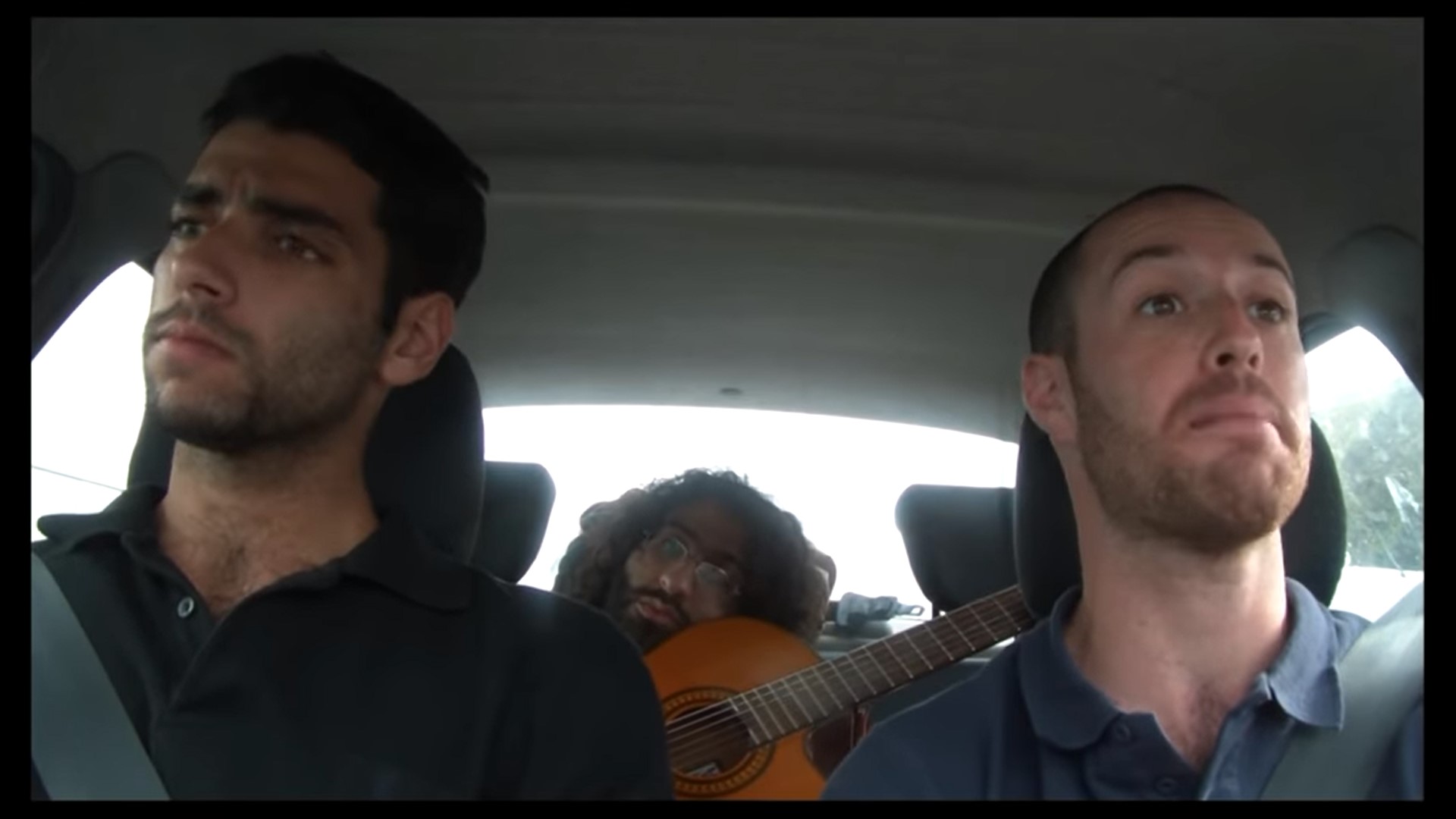 שלושה גברים באוטו, אחד מאחורה עם גיטרה