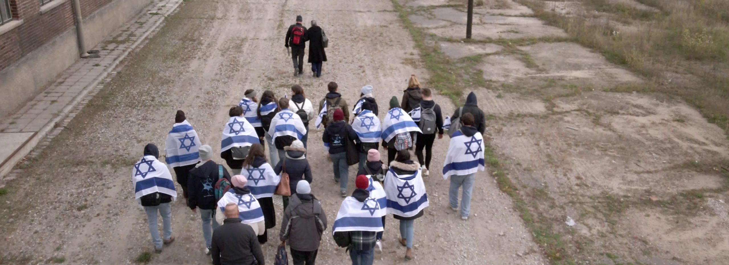 קבוצת נערים עטופים בדגלי ישראל צועדים על שבילים ומולם הולכים המדריך והניצולה