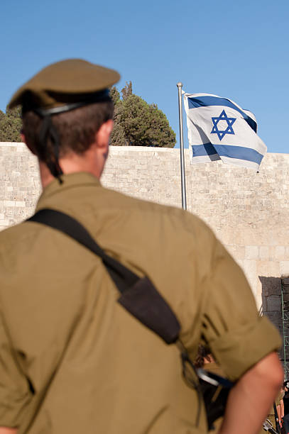 גב של חייל צה"ל במדים עם כומתה על הראש, מסתכל לכיוון דגל ישראל שמונף על תורן