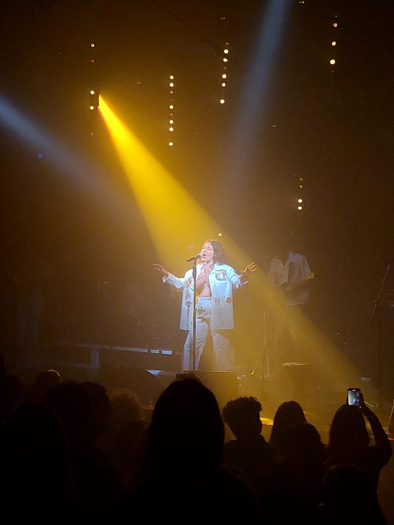זמרת על הבמה לבושה לבן, זרקור צהוב-כתום מאיר עליה